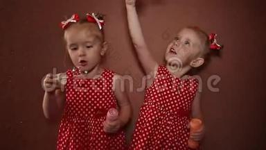 两个漂亮的双胞胎姐<strong>妹</strong>穿着漂亮的红色连衣裙，在房子的房间里一起吹<strong>肥</strong>皂泡。